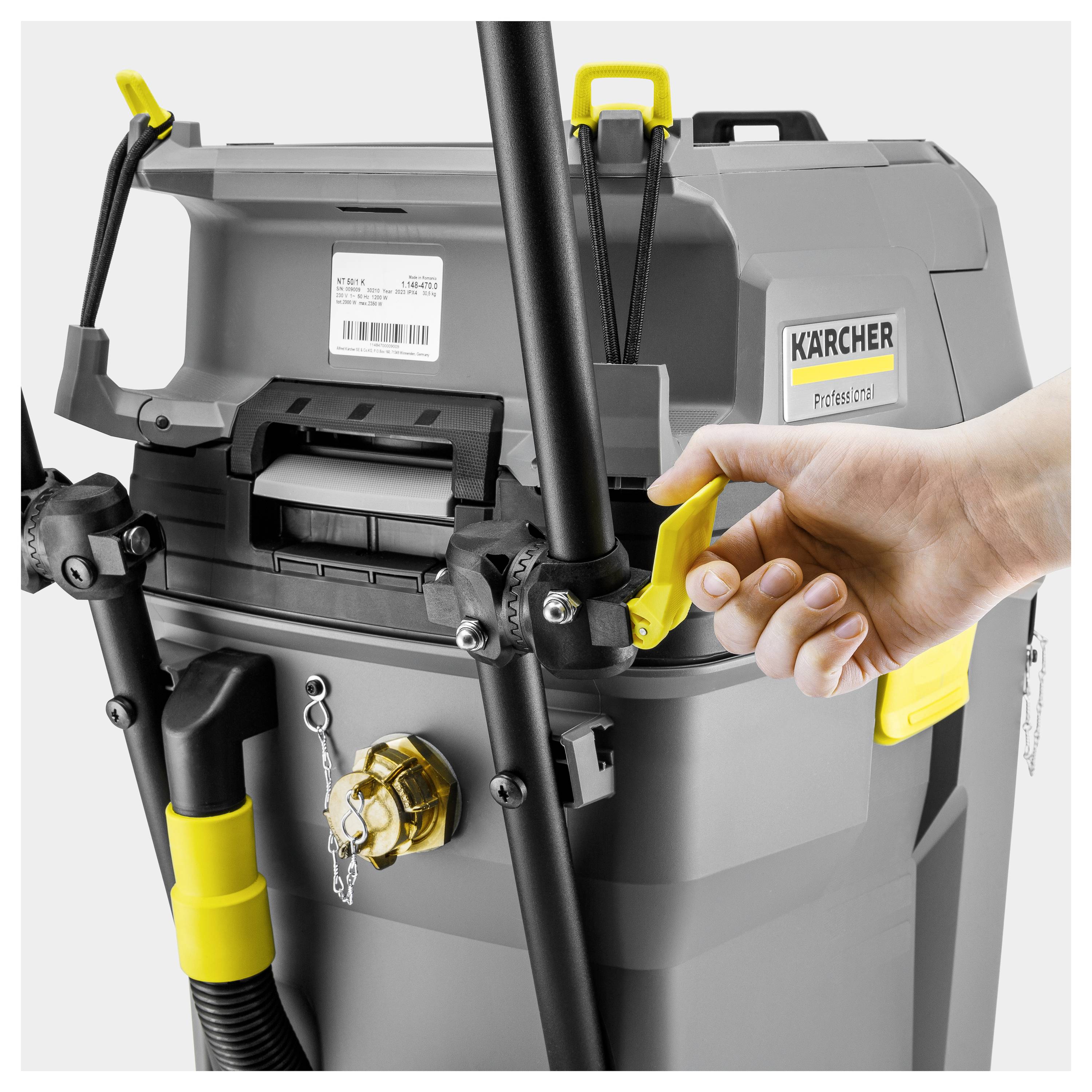 Eine Person öffnet einen grauen Industrialstaubsauger von Kärcher mit einem gelben Riegel, umgeben von schwarzen und gelben Aufsätzen.