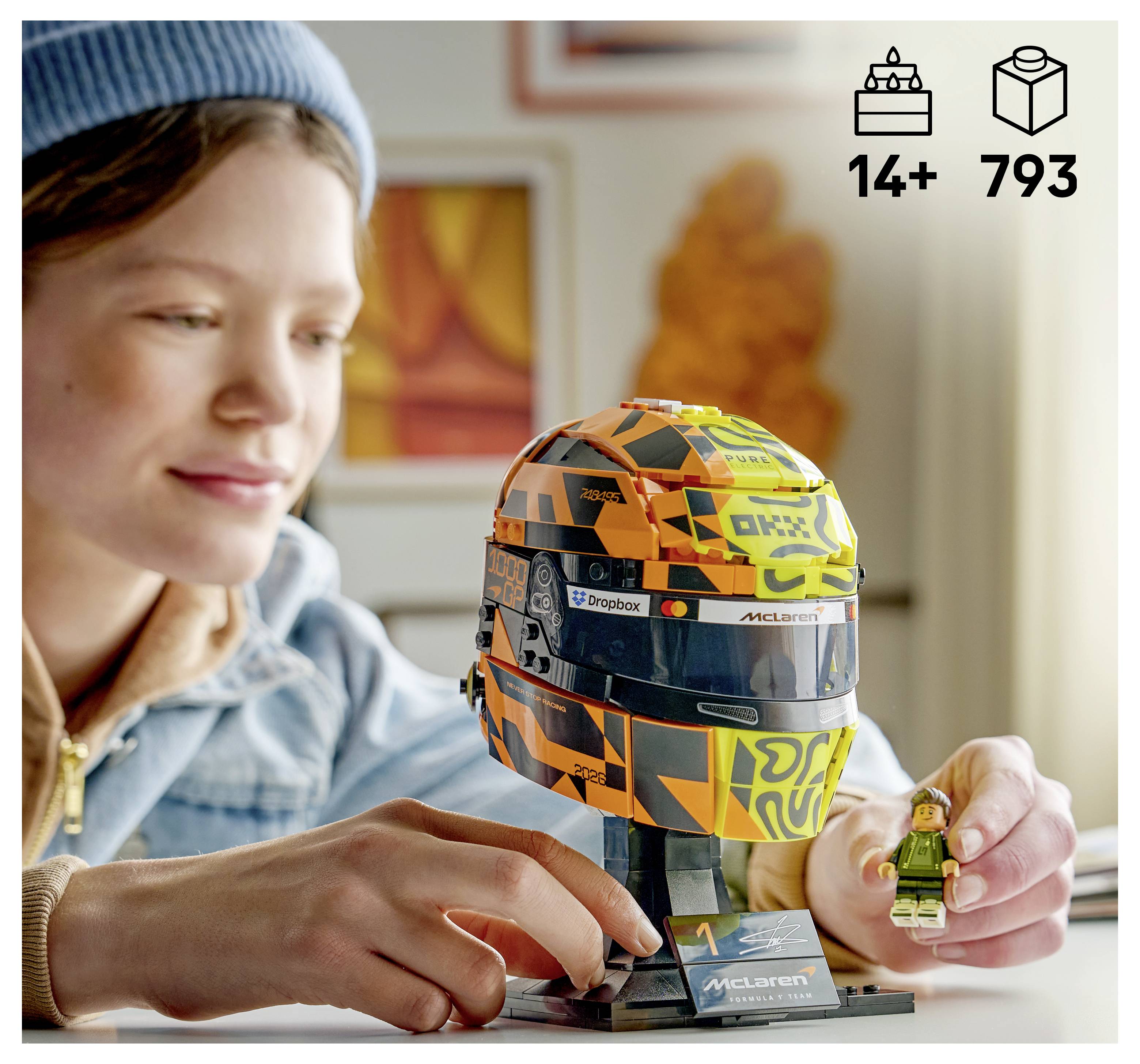 Ein Kind baut ein LEGO McLaren Formel-1-Helm-Modell zusammen, wobei eine Minifigur enthalten ist; Die Schachtelvorderseite zeigt das Alter 14+ und 793 Teile.