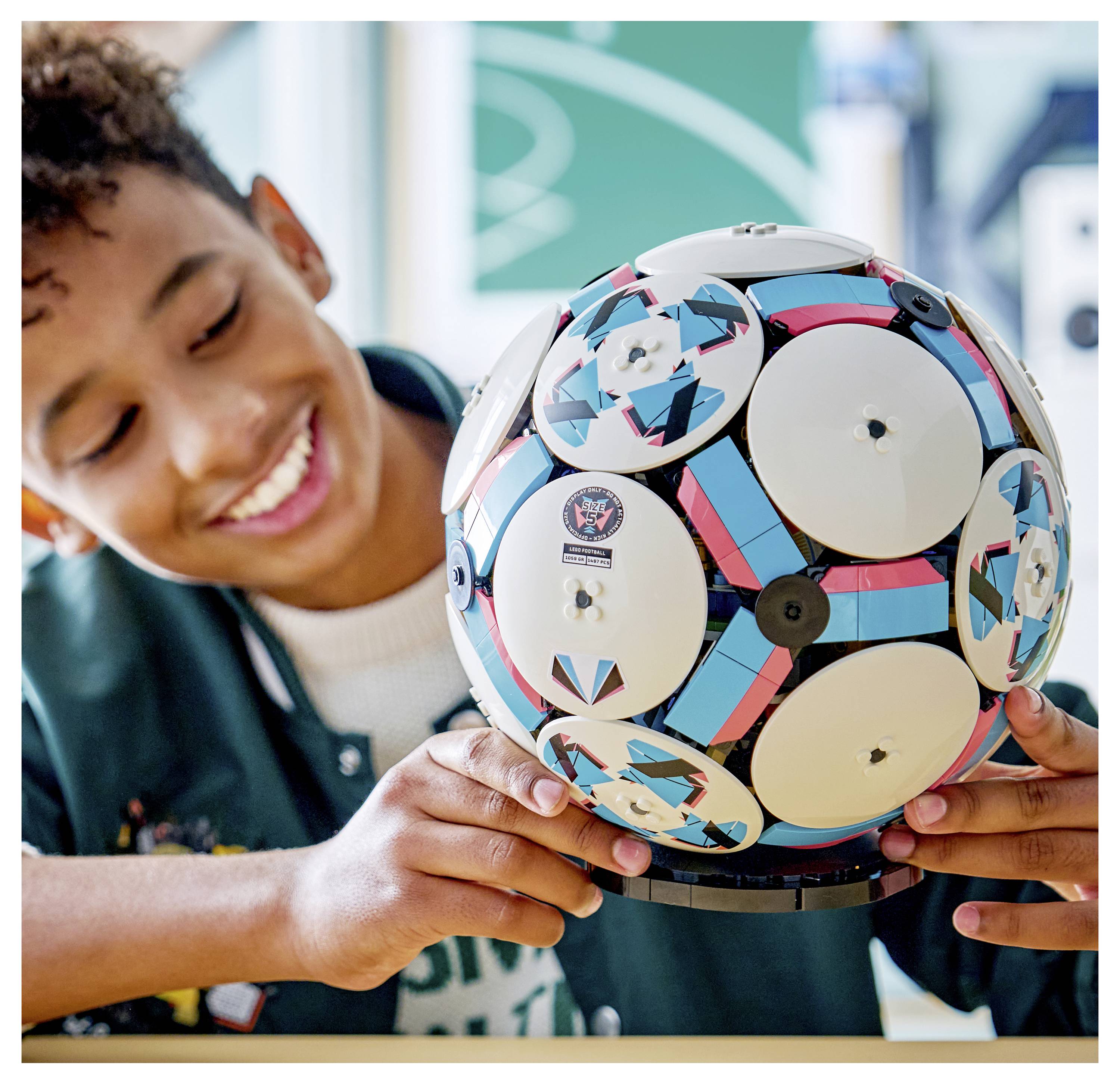 Eine Person, die lächelt, während sie eine bunte, geometrische Sphäre mit verschiedenen Mustern und Designs hält, die ein Gefühl von Kreativität und Freude ausstrahlt.