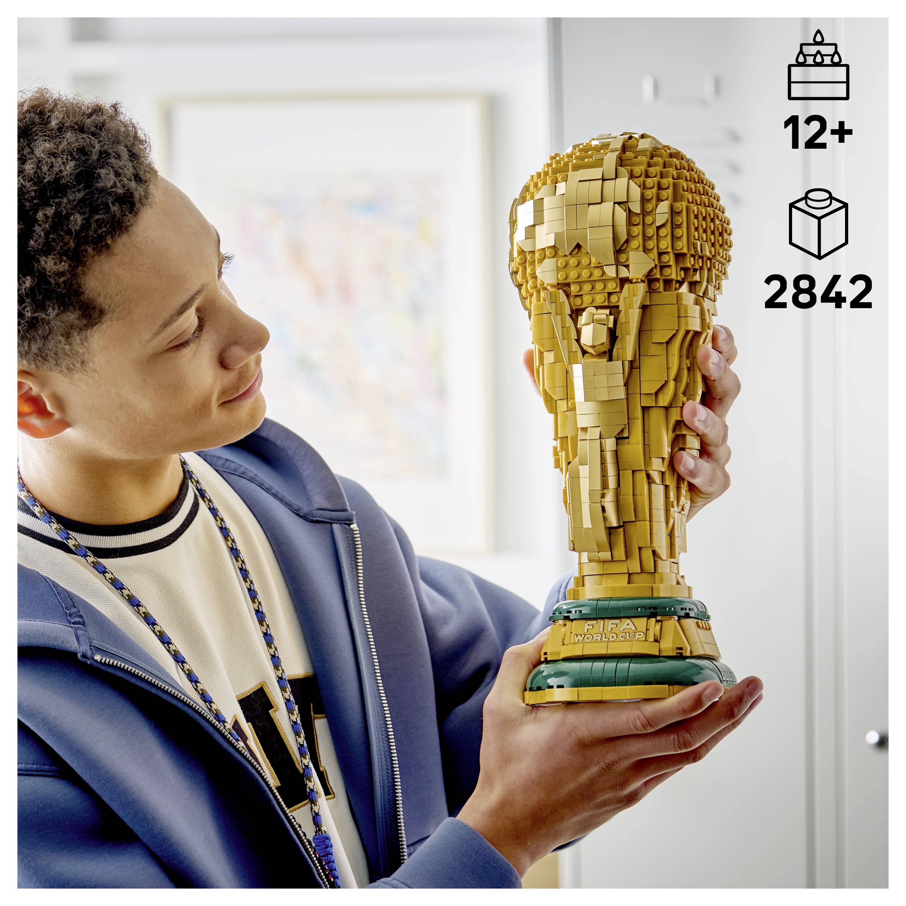 Eine Person hält eine detaillierte LEGO-Trophäe, die einem Pokal aus Gold ähnelt. Das Set ist für Altersgruppen ab 12 Jahren geeignet und enthält 2.842 Teile.