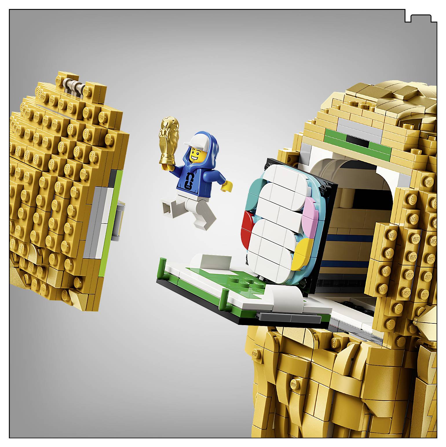 Eine LEGO-Figur mit einem blauen Hoodie springt von einer goldenen Apfelstruktur herunter und hält dabei eine goldene Trophäe.