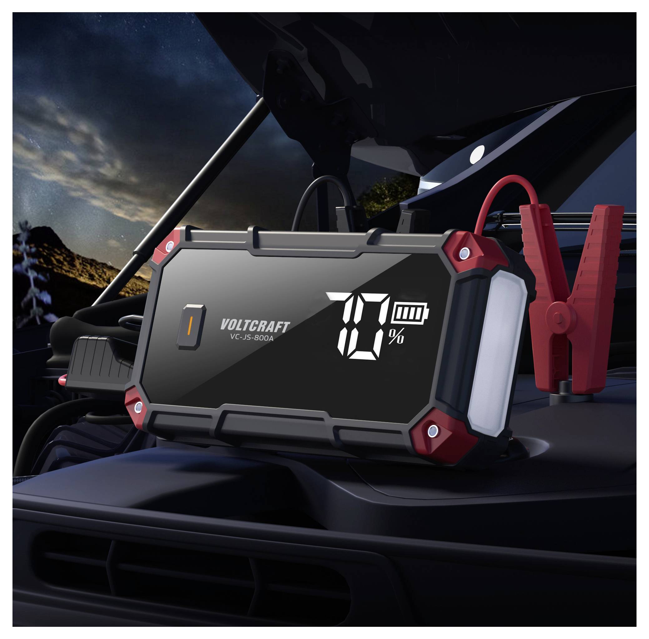 Tragbares VOLTCRAFT-Autobatterieladegerät/Starthilfegerät auf der Motorhaube eines Fahrzeugs, zeigt 70% Ladezustand an, mit roten Klemmen angebracht.