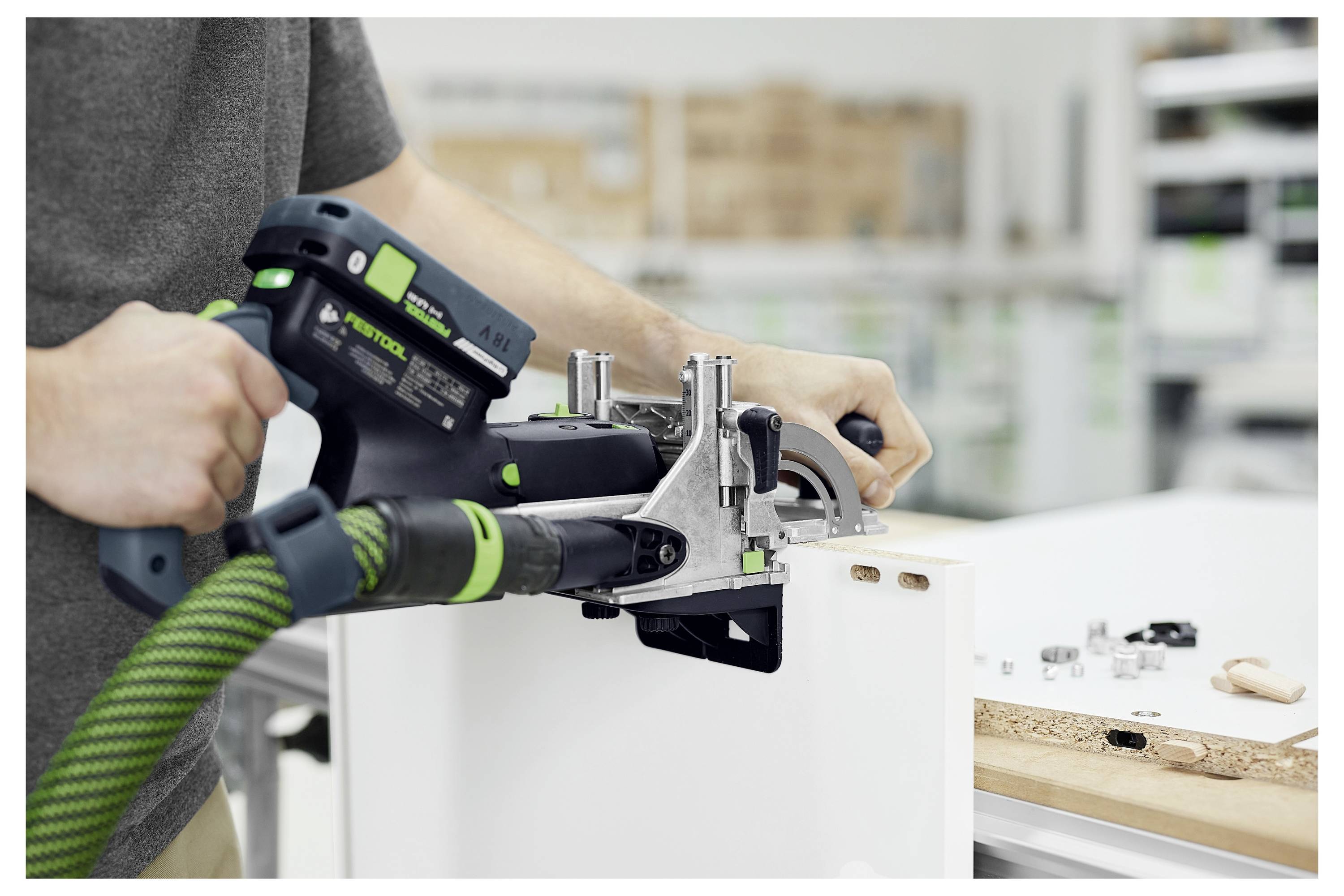 Ein Mann in einem schwarzen Poloshirt hält einen kabellosen Bohrer mit konzentriertem Gesichtsausdruck. Er steht draußen in der Nähe eines Gebäudes unter Konstruktion.