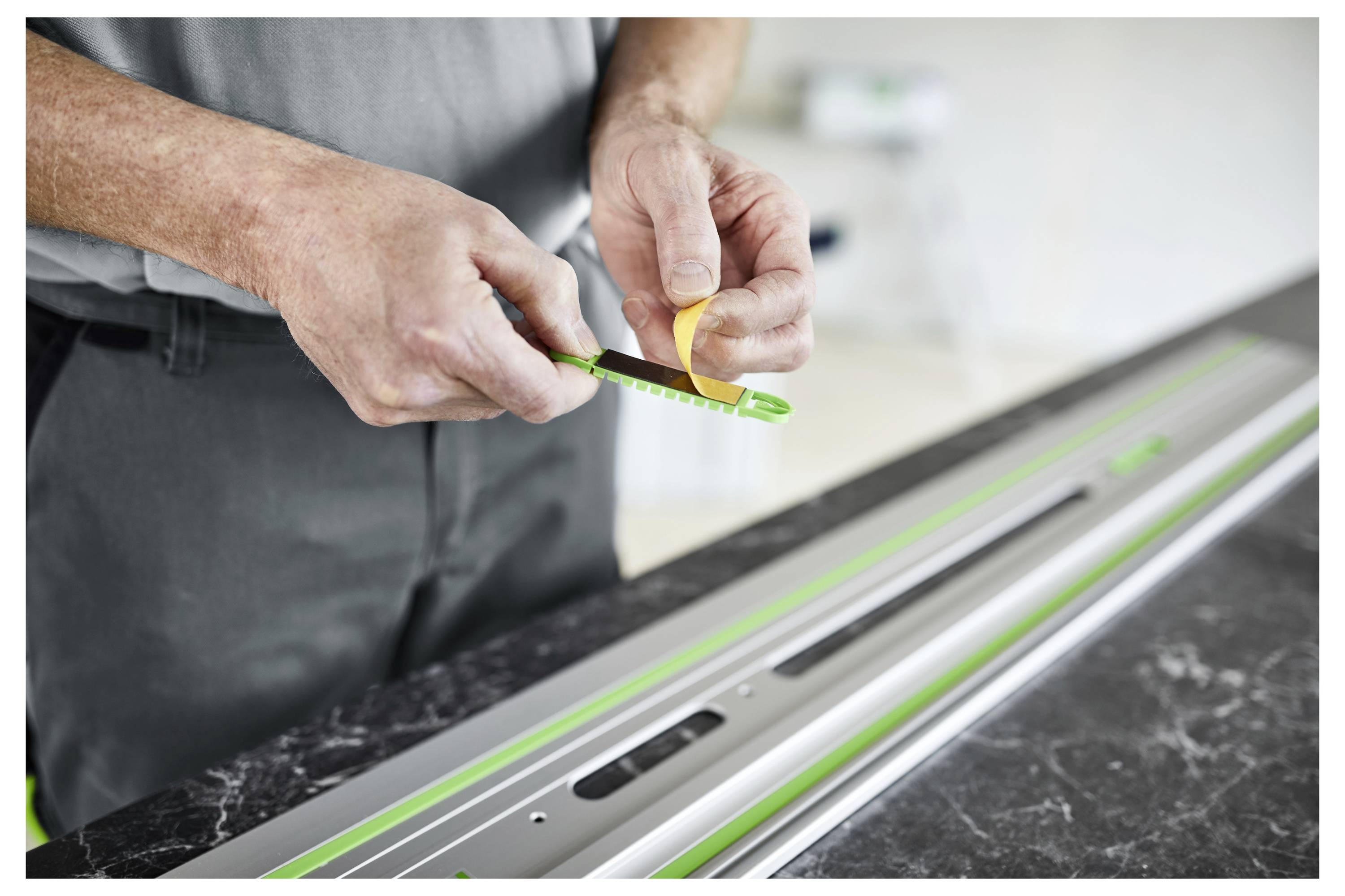 Ein schwarzer und grüner Festool-Router auf einer Werkbank, umgeben von Holzstücken und einer Führungsschienen-Anlage, verwendet für präzise Holzbearbeitung.