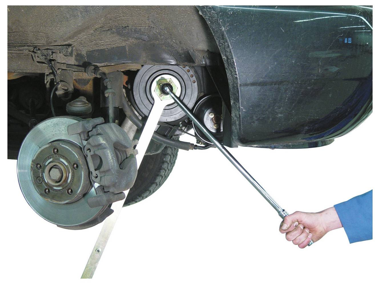 Ein Mechaniker verwendet einen Drehmomentschlüssel, um eine hintere Radnabe an einem Fahrzeug einzustellen, wobei die Bremsscheibe und der Bremssattel sichtbar sind.