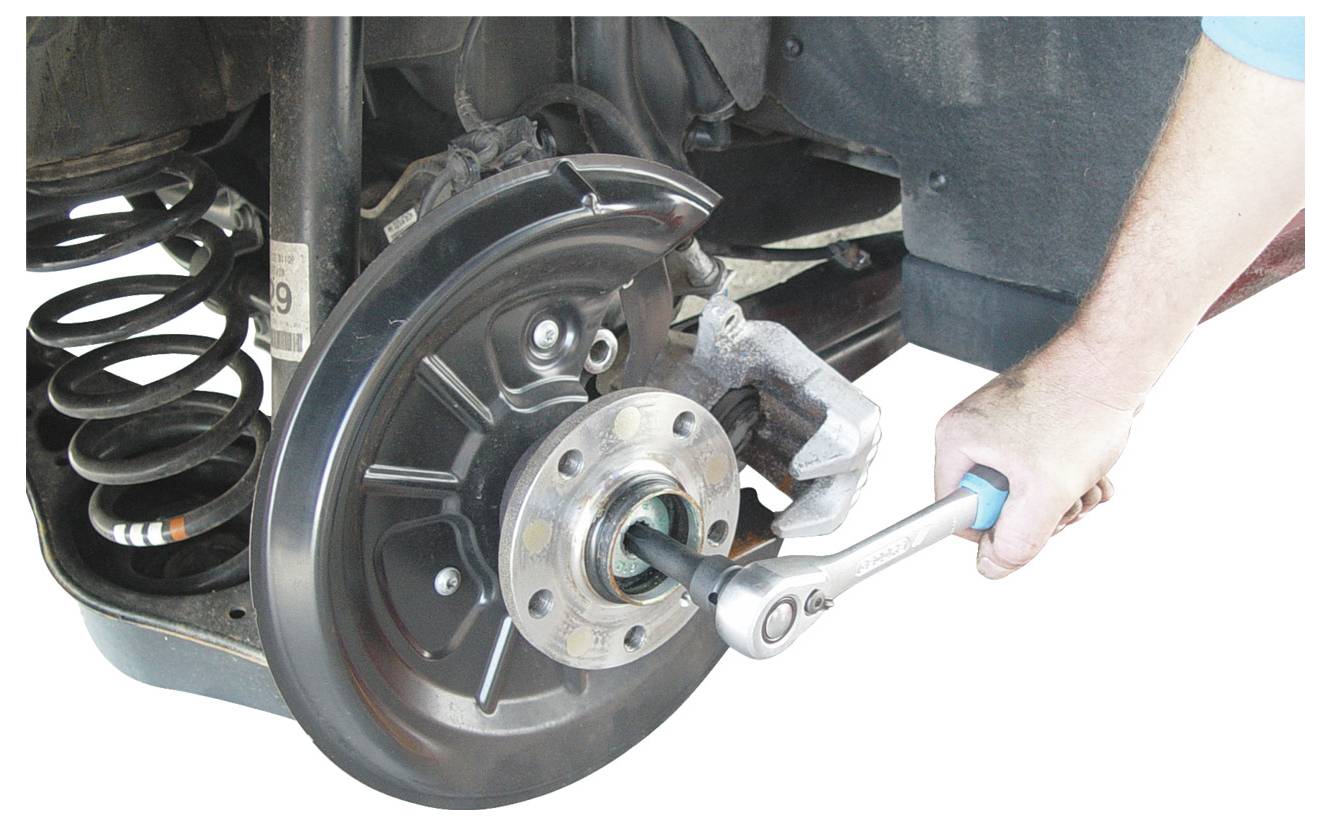 Ein Mechaniker verwendet einen Ratschenschlüssel, um an der Radnabe und dem Aufhängungssystem eines Autos zu arbeiten, was Verfahren zur Autoreparatur veranschaulicht.
