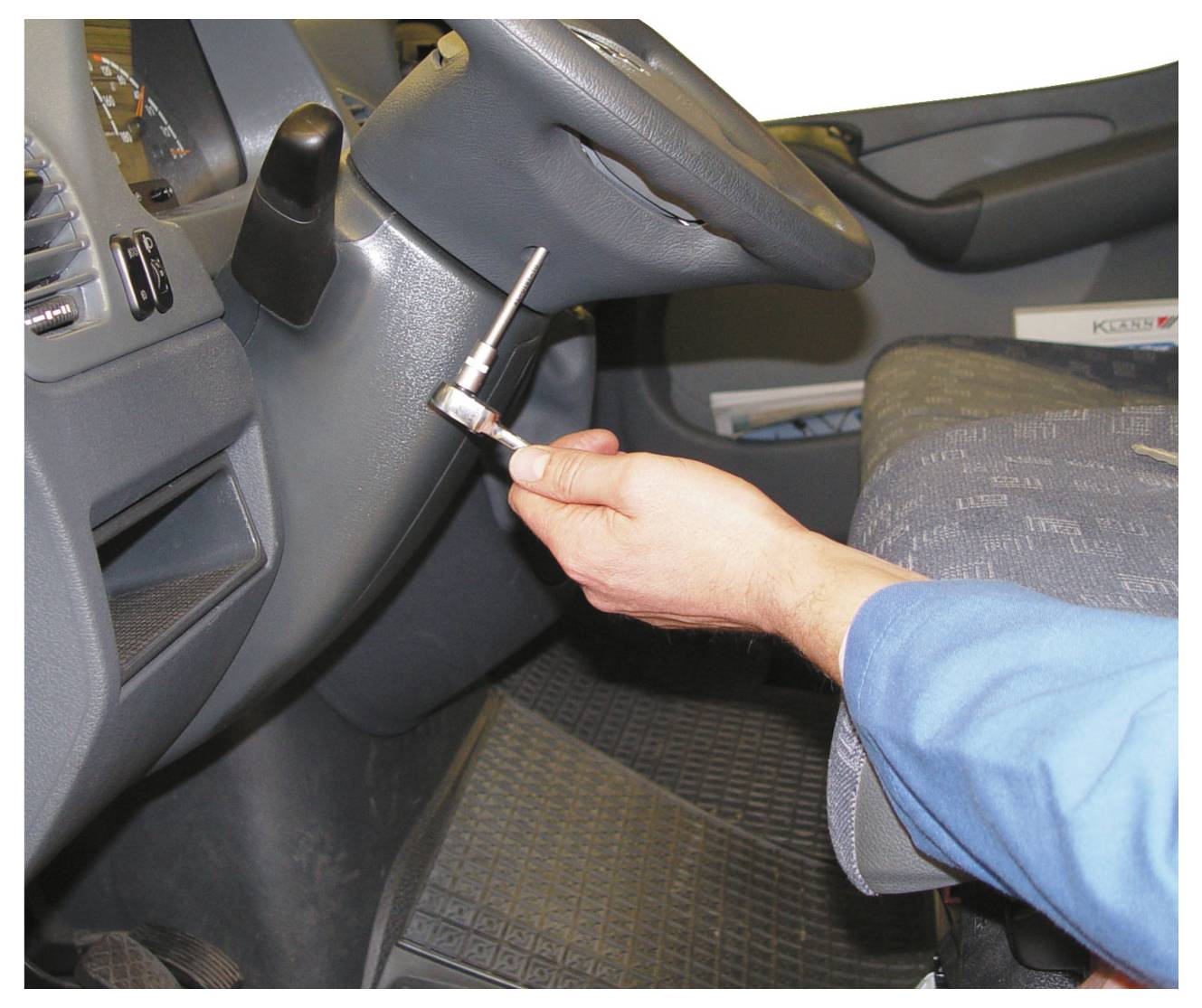 Eine Person in einem blauen Hemd verwendet einen Ratschenschlüssel, um einen Bolzen in der Nähe des Lenkrads eines Autos anzupassen, möglicherweise um Wartungsarbeiten durchzuführen.