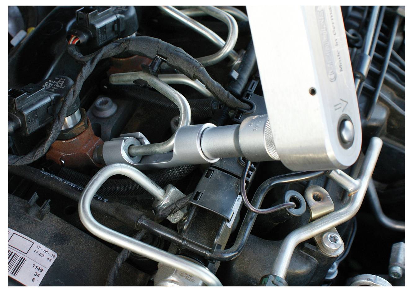 Ein Drehmomentschlüssel zieht eine Schraube an einem Automotor an, wobei sichtbare Metallrohre und Drähte den Bereich umgeben.