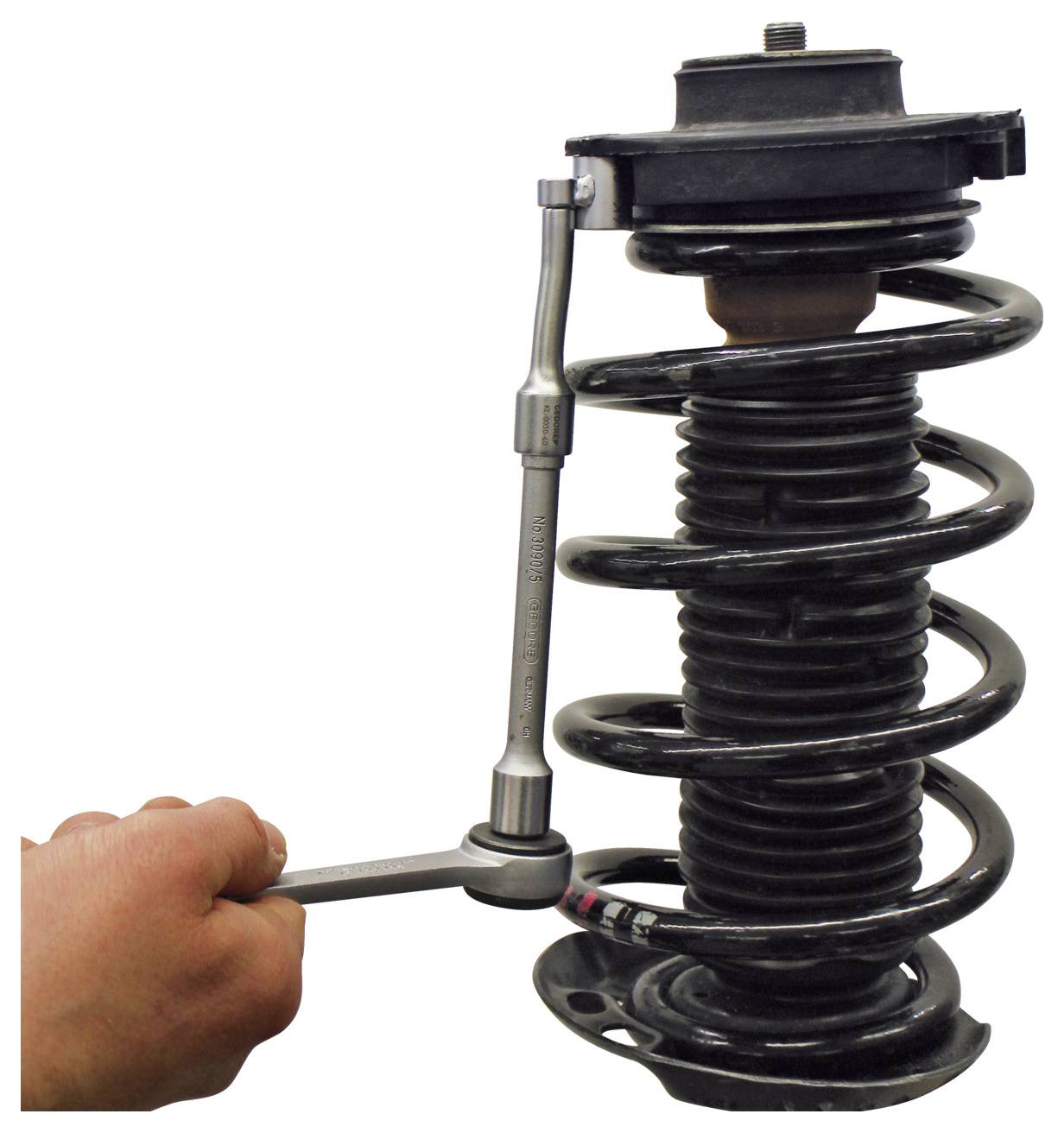 Eine Hand, die einen Schraubenschlüssel verwendet, um ein Federbeinsystem eines Autos einzustellen, was einen Teil eines Fahrzeugwartungsprozesses demonstriert.