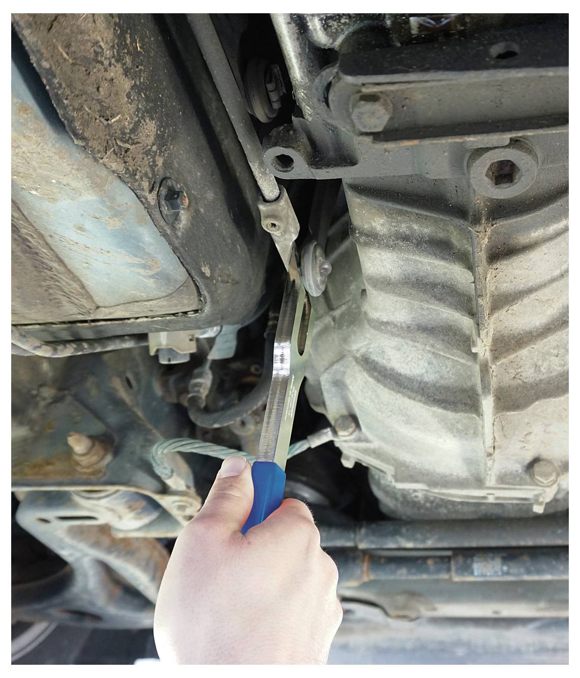 Eine Person verwendet einen Schraubenschlüssel, um Bolzen in der Unterseite eines Autos anzuziehen, wobei der Fokus auf mechanischen Reparaturen und Wartung liegt.