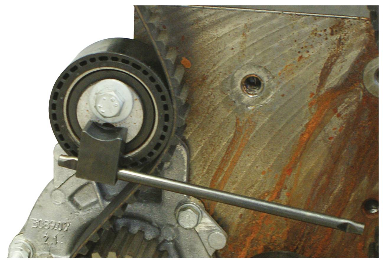 „Nahaufnahme eines Maschinenteils einer Industriemaschine, das ein Zahnrad und ein Rad zeigt, mit einer Metallstange, die darüber gelegt ist. Der Hintergrund ist eine rostige Oberfläche.