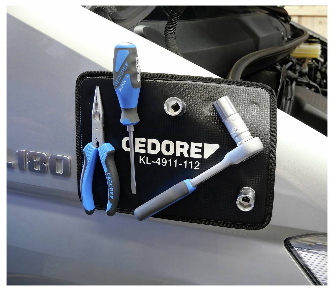 Eine magnetische Werkzeugmatte mit einem Schraubendreher, einer Zange und einem Steckschlüssel ist an der Motorhaube eines Autos angebracht und trägt das Etikett „GEDORE KL-4911-112
