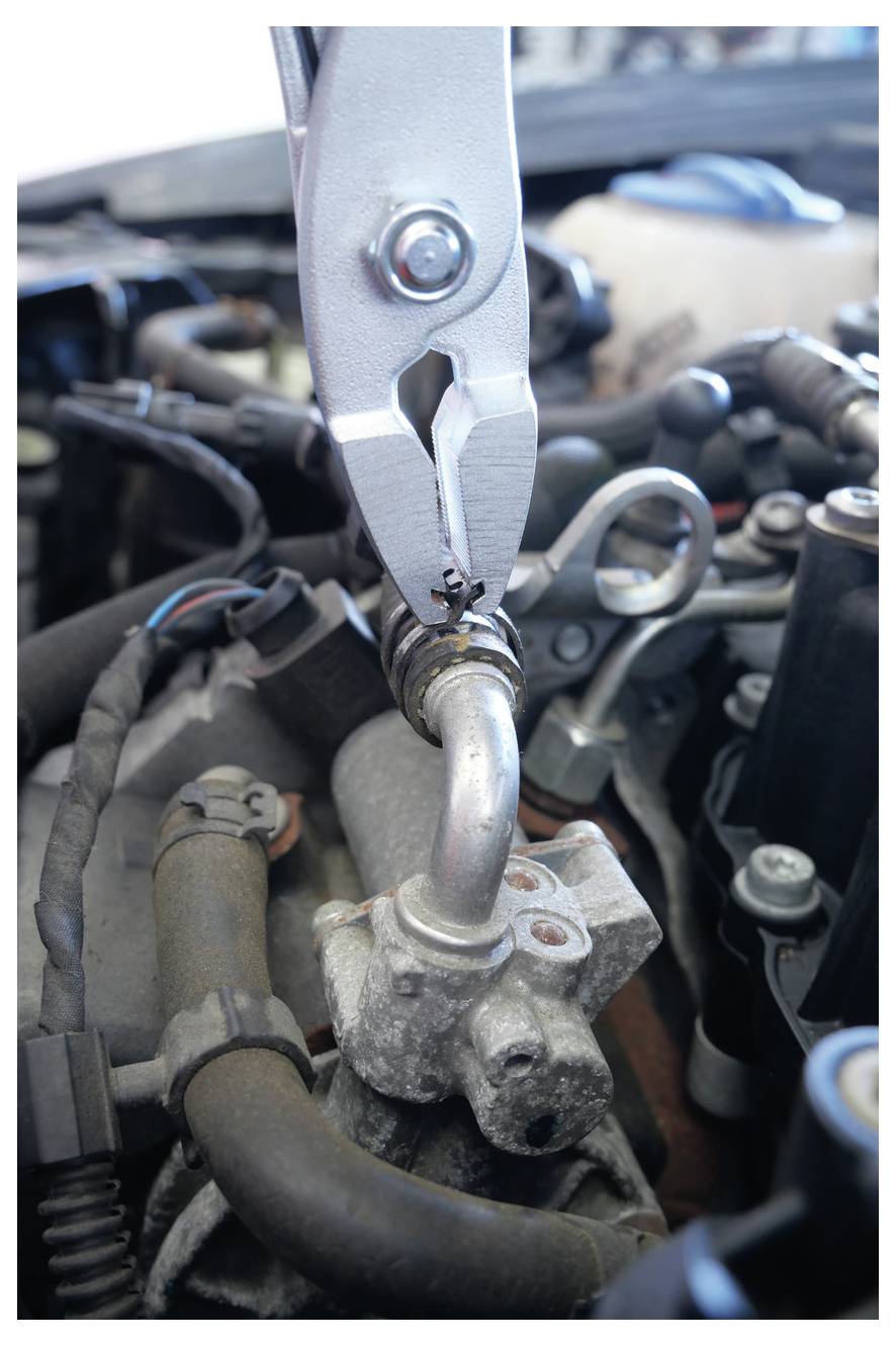 Nahaufnahme einer Zange, die ein Metallrohr in einem Automotor greift, wobei Reparaturarbeiten an Fahzeugkomponenten hervorgehoben werden.