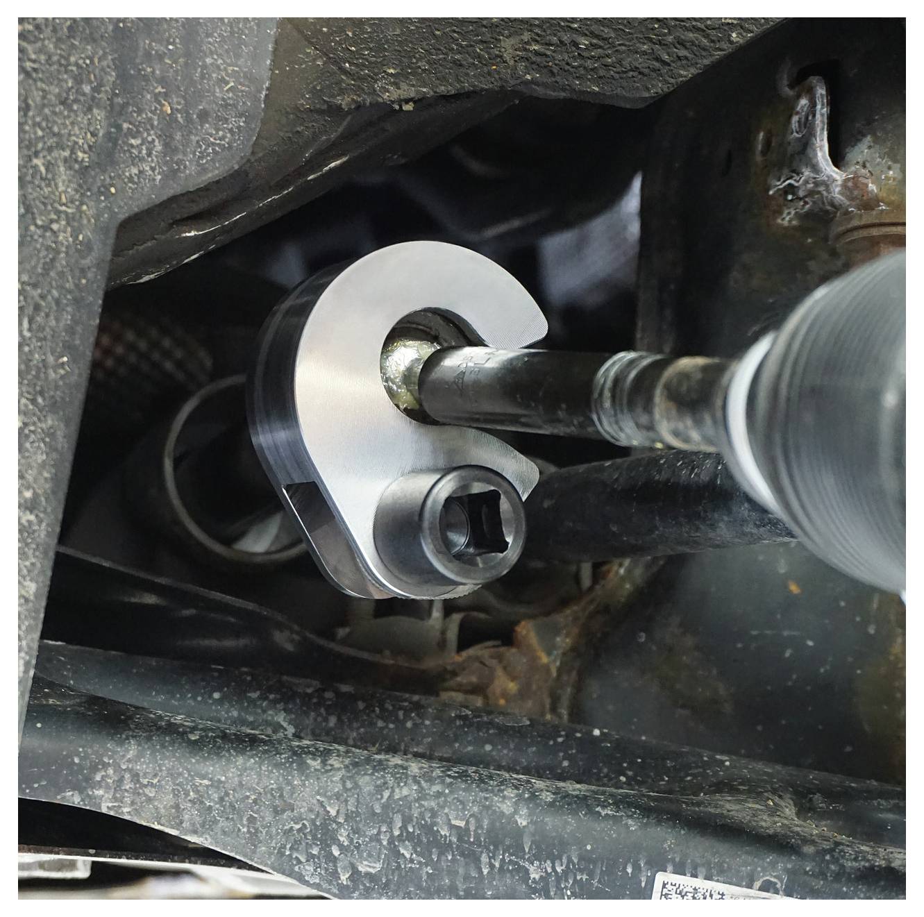 Ein C-förmiger Drehmomentschlüssel wird an einem Querlenker-Bolzen eines Fahrzeugs verwendet und zeigt die Werkzeugeinsatz für präzises Anziehen.