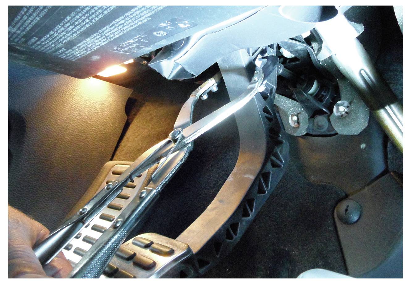 Ein weißes Auto wird auf einer Hebebühne in einer Garage hochgefahren, mit einer blauen Gedore-Werkzeugkiste im Vordergrund. Die Kiste hat offene Schubladen, die verschiedene Werkzeuge zeigen.