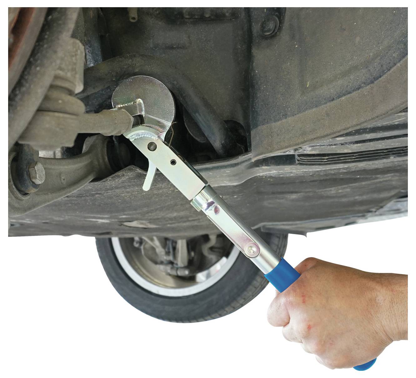Eine Hand benutzt ein Werkzeug mit blauem Griff, um den Ölfilter eines Autos zu greifen, um ihn zu entfernen oder einzubauen, wobei ein Rad im Hintergrund sichtbar ist.