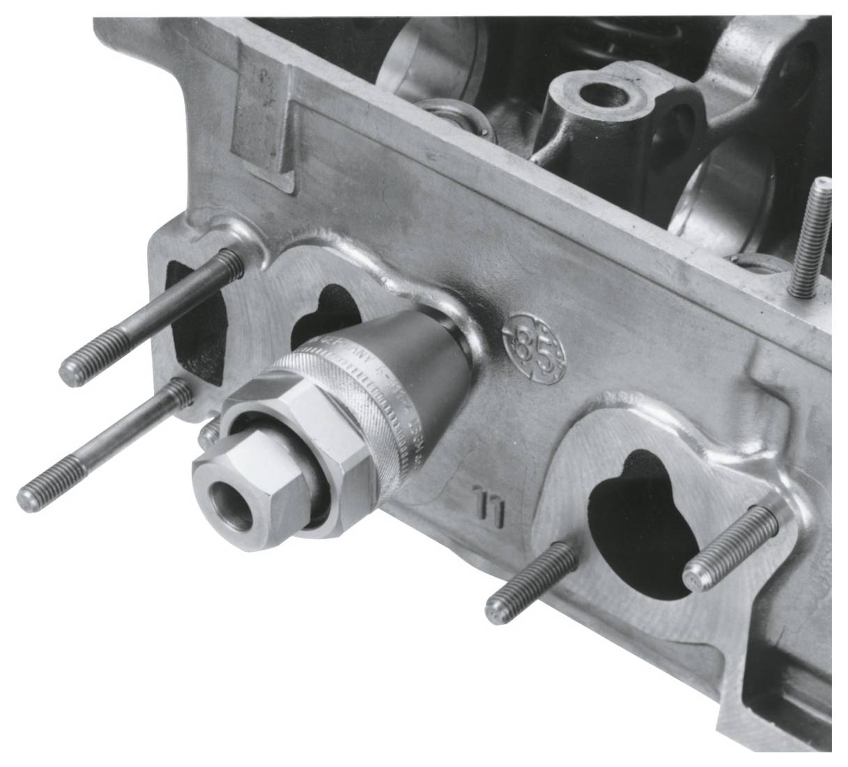 Nahaufnahme eines Motorblocks mit sichtbaren Bolzen und einer Metallarmatur, die mechanische Komponenten eines Verbrennungsmotors zeigt.