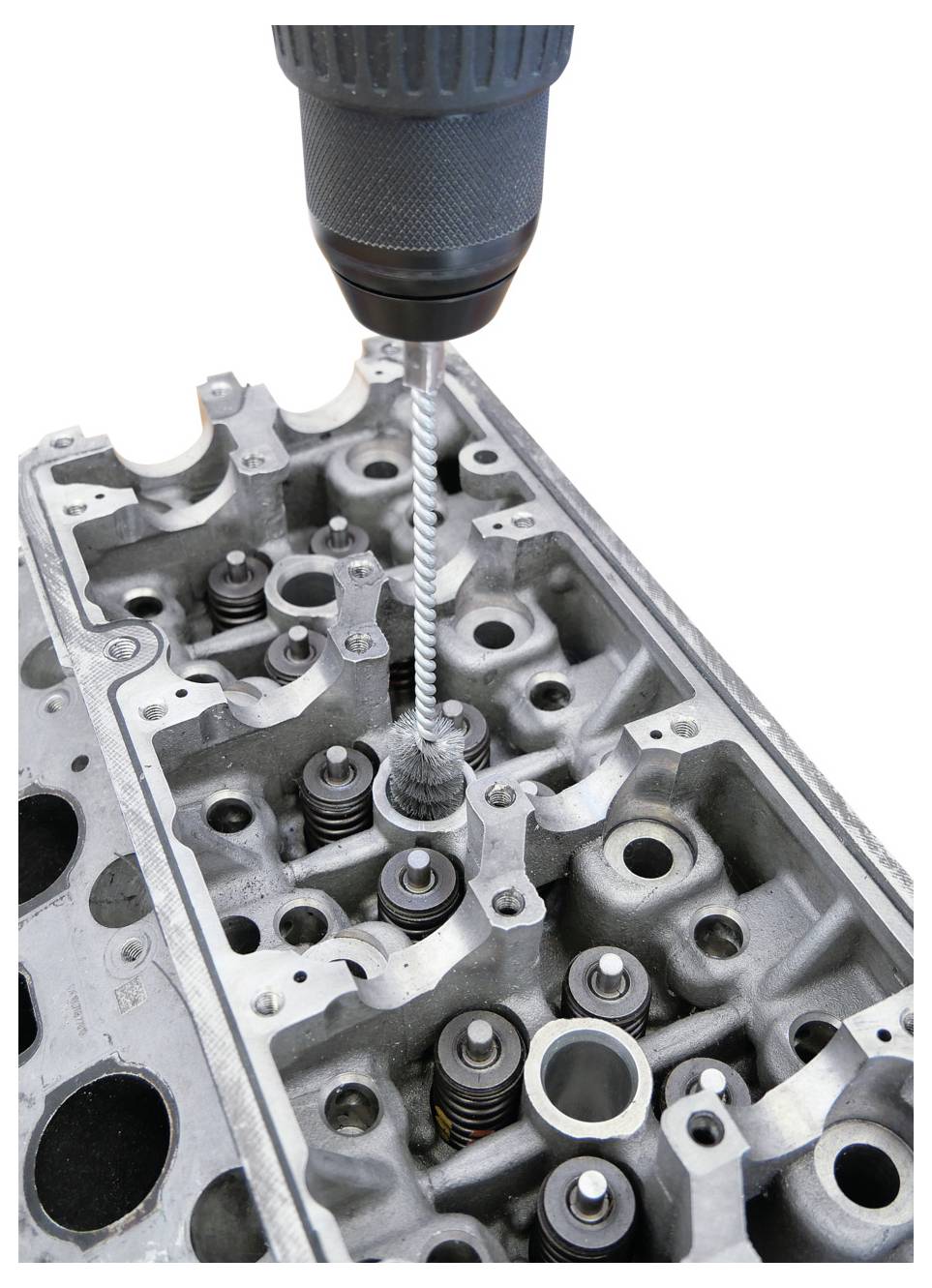 Eine Nahaufnahme eines Bohrers, der Gewinde in einen Motorblock schneidet. Der Bohrer ist über der metallischen Motoroberfläche positioniert, wobei sichtbare Ventilkomponenten erkennbar sind.