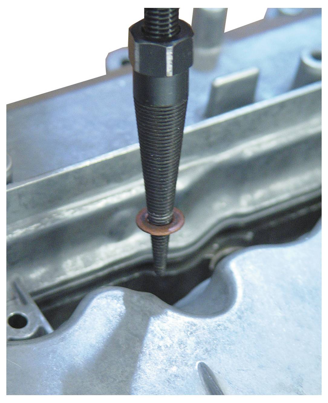 Nahaufnahme einer Gewindestange mit einer roten Unterlegscheibe, die eine metallische Oberfläche durchdringt, was einen mechanischen Montage- oder Reparaturprozess veranschaulicht.