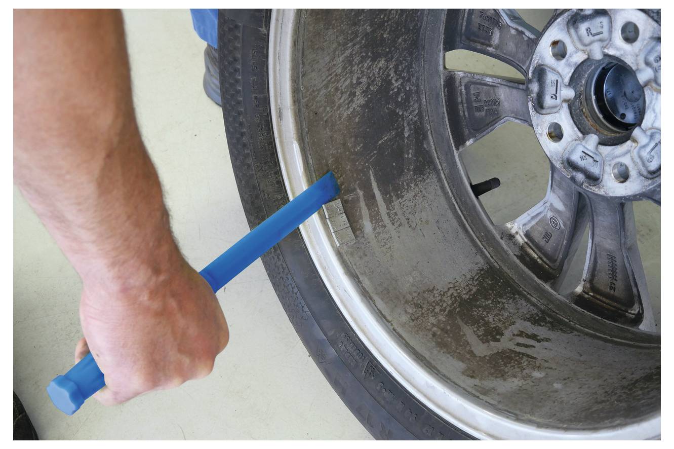 Eine Person hält eine blaue Brechstange, um ein Radgewicht von einer verschmutzten Autofelge zu entfernen.