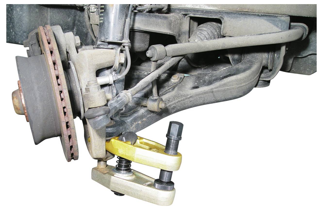 Nahaufnahmebild eines Fahzeugsuspensionssystems, das ein Kugelgelenkabzieher-Werkzeug in Verwendung zeigt und fahrzeugwartung oder -reparatur demonstriert.