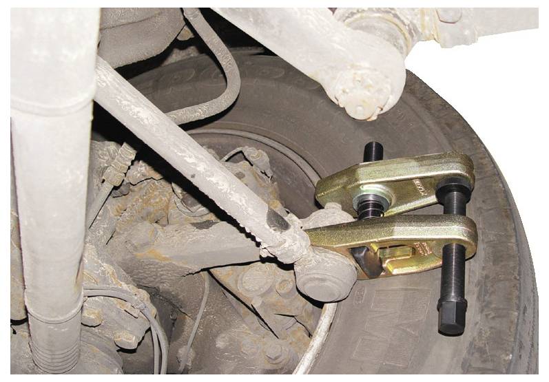 Ein Aufhängungssystem eines Fahrzeugs mit einem angebrachten Kugelgelenkabzieher, das eine Nahaufnahme der mechanischen Komponenten und verrosteten Bereiche zeigt.