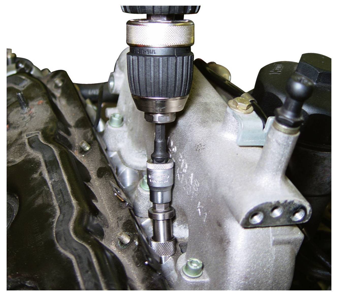 Ein Elektroschrauber zieht einen Bolzen an einem Metallmotorblock fest und demonstriert die Werkzeugnutzung bei mechanischer Wartung oder Reparatur.