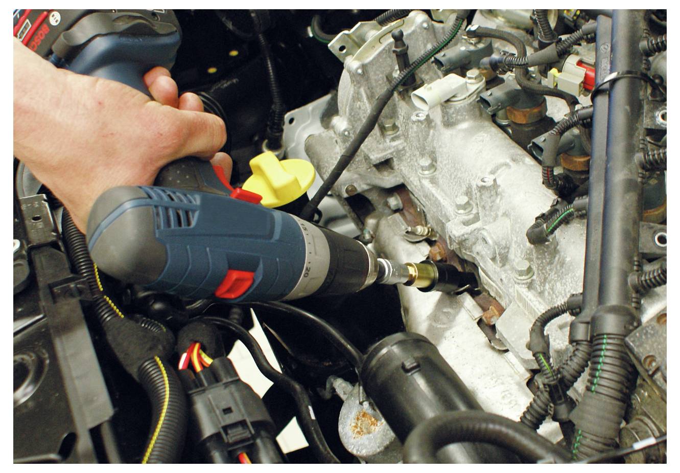 Eine Hand benutzt eine Elektrobohrermaschine, um einen Bolzen an einem Automotor festzuziehen, zeigt Wartungs- oder Reparaturarbeiten am Fahrzeug in Arbeit.