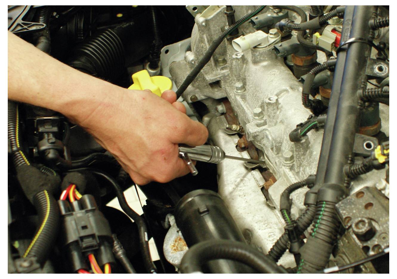 Eine Person, die ein Werkzeug verwendet, um einen Teil eines Motors einzustellen oder zu reparieren, umgeben von verschiedenen Autoteilen und Kabeln, was auf Automobilwartung hindeutet.