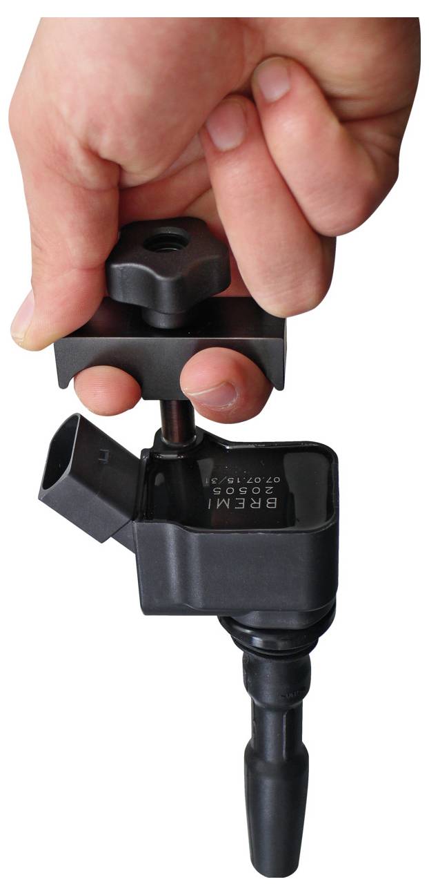 Eine Hand, die ein Werkzeug verwendet, um eine Zündspule aus einem Fahrzeugmotor zu entfernen, und zeigt dabei den Extraktionsprozess für Wartung oder Reparatur.