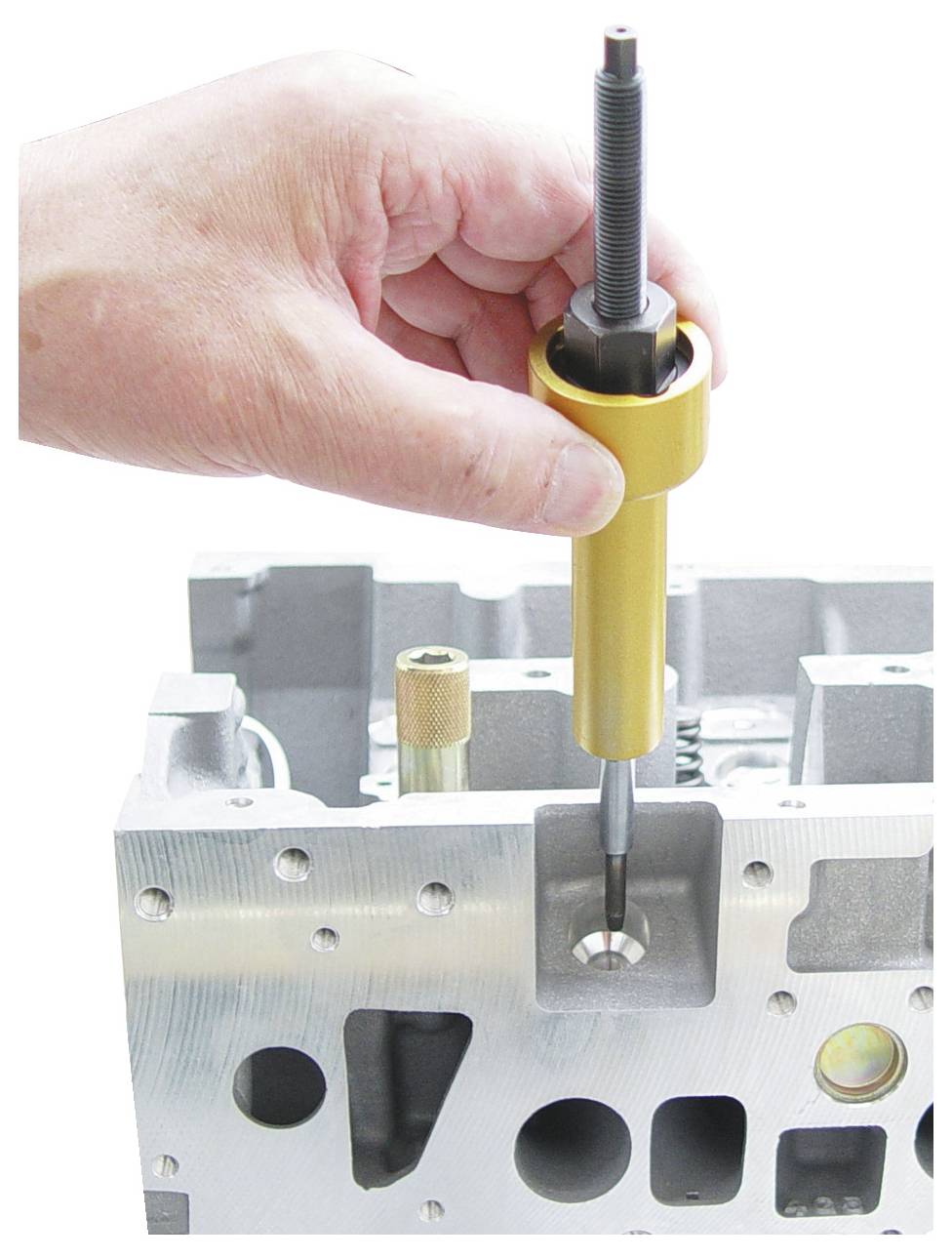 Hand mit einem Werkzeug, das eine Ventilführung in einem Automotorenblock installiert.
