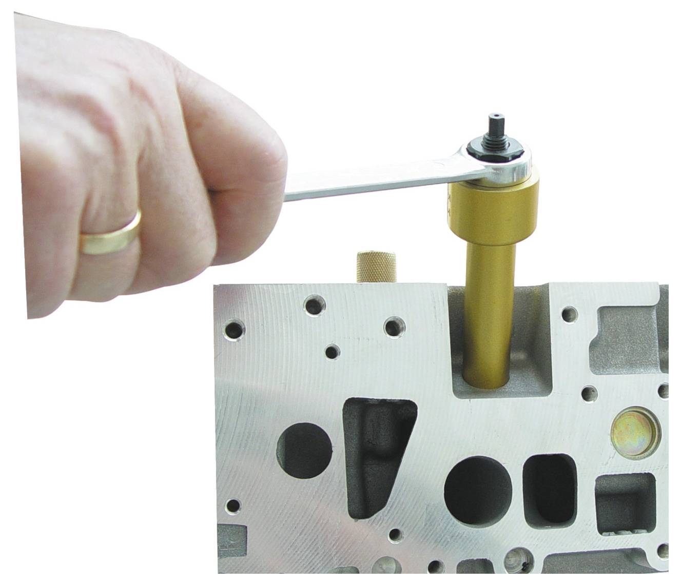 Eine Hand benutzt einen Schraubenschlüssel, um eine Komponente auf einem Metallmotorblock einzustellen, was einen Wartungs- oder Reparaturprozess veranschaulicht.