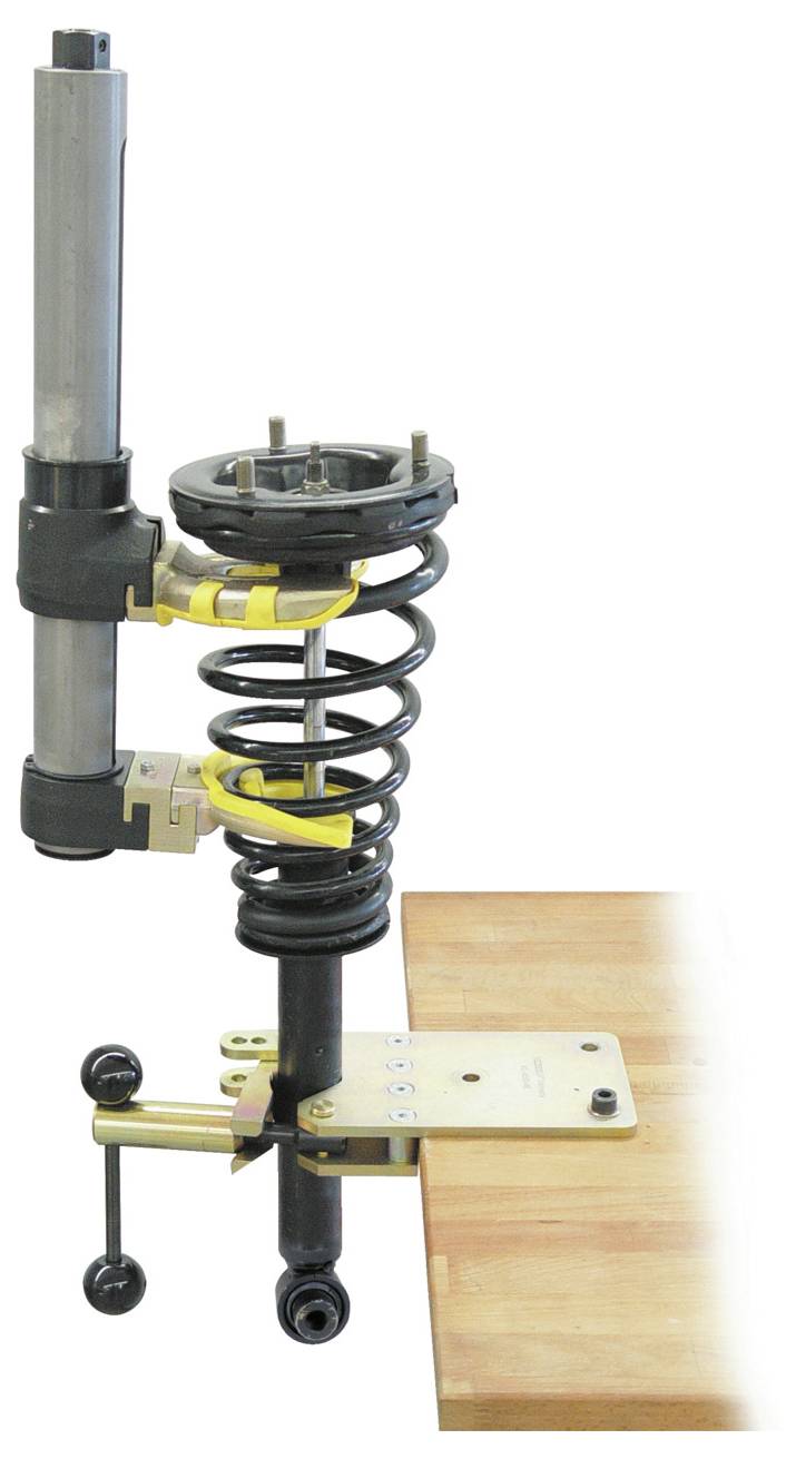 Ein auf einer Holzwerkbank befestigter Spannwerkzeugsatz für Federungslängslenker, der verschiedene Komponenten wie Federn und Spannzangen zeigt.