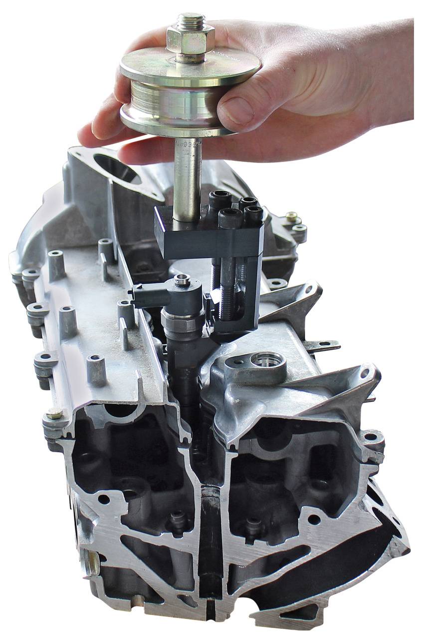 Eine Hand hält ein silberfarbenes Werkzeug über ein Metall-Motorenteil und demonstriert möglicherweise die Wartung oder Montage des Motorenbauteils.