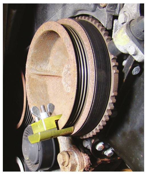 Das Bild zeigt eine Nahaufnahme einer rostigen Motorriemenscheibe mit einem angebrachten Spannwerkzeug. Die Riemenscheibe verfügt über ein Mehrnutdesign.