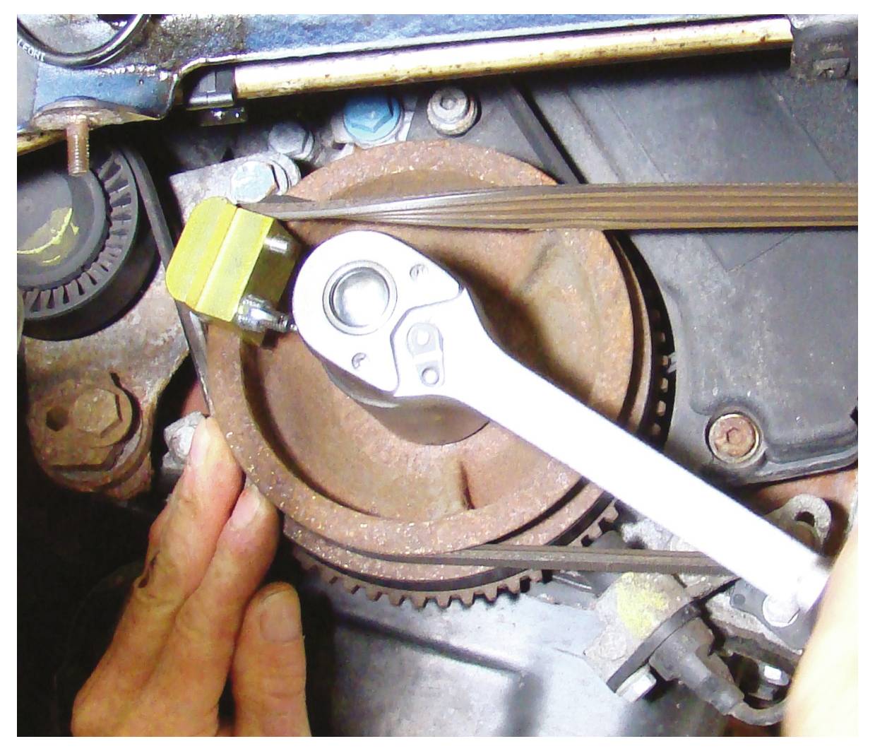Eine Hand, die einen Schraubenschlüssel an einem Automotor-Riemen verwendet und eine Schraube an einer Riemenscheibe anpasst.