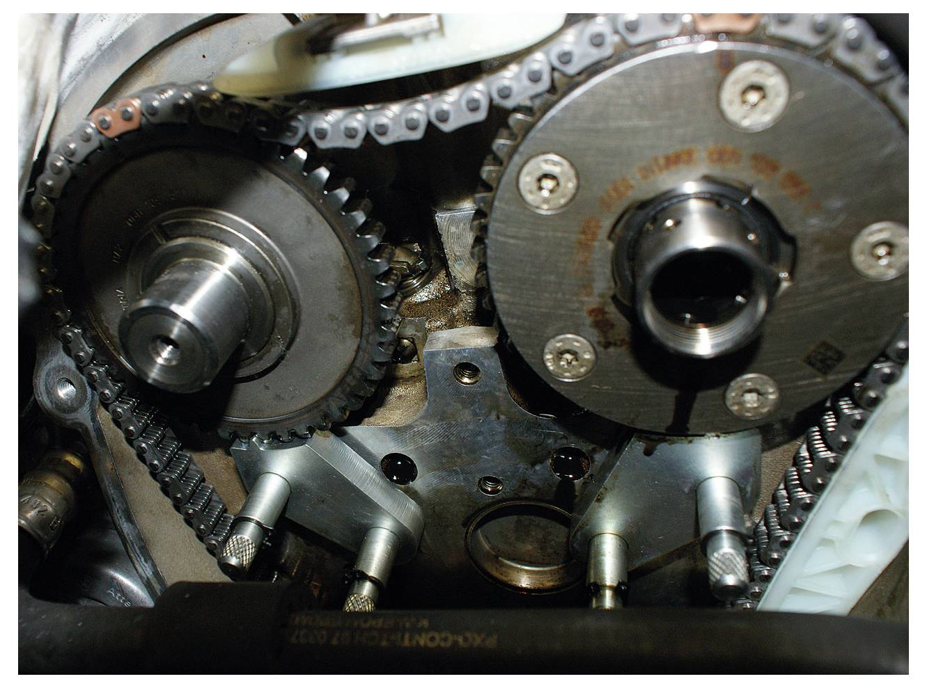 Nahaufnahme der Steuerkettenbaugruppe eines Automotors, die Zahnräder und ineinander verschlungene Ketten zeigt und deren mechanische Struktur hervorhebt.