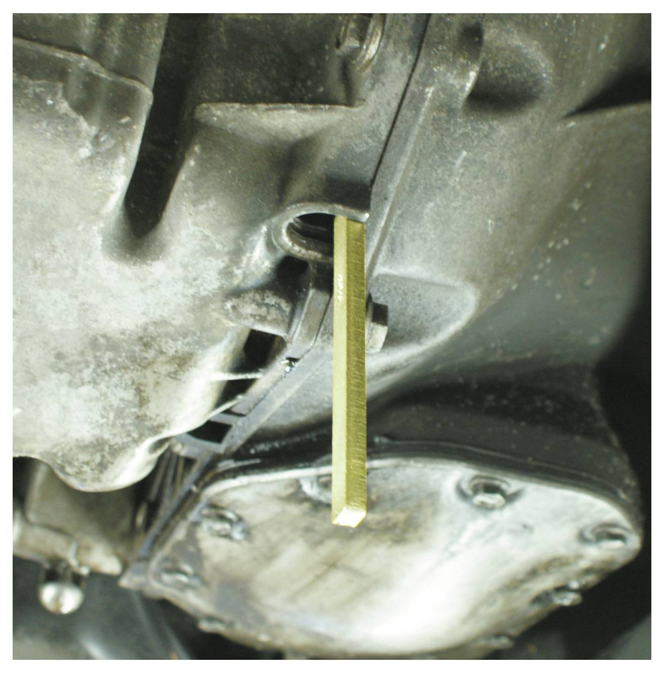 Ein metallischer rechteckiger Ölmessstab, der in die Seite eines Motorblocks eingeführt wird, um den Ölstand zu messen, mit sichtbaren verschmutzten Motoroberflächen.