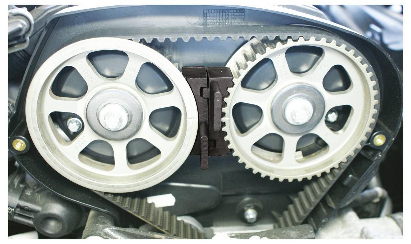 Ein Zahnriemensystem für einen Motor, das zwei graue Zahnräder zeigt, die durch einen Gummiriemen verbunden sind, der für die Synchronisierung der Nockenwelle und der Kurbelwelle des Motors wesentlich ist.