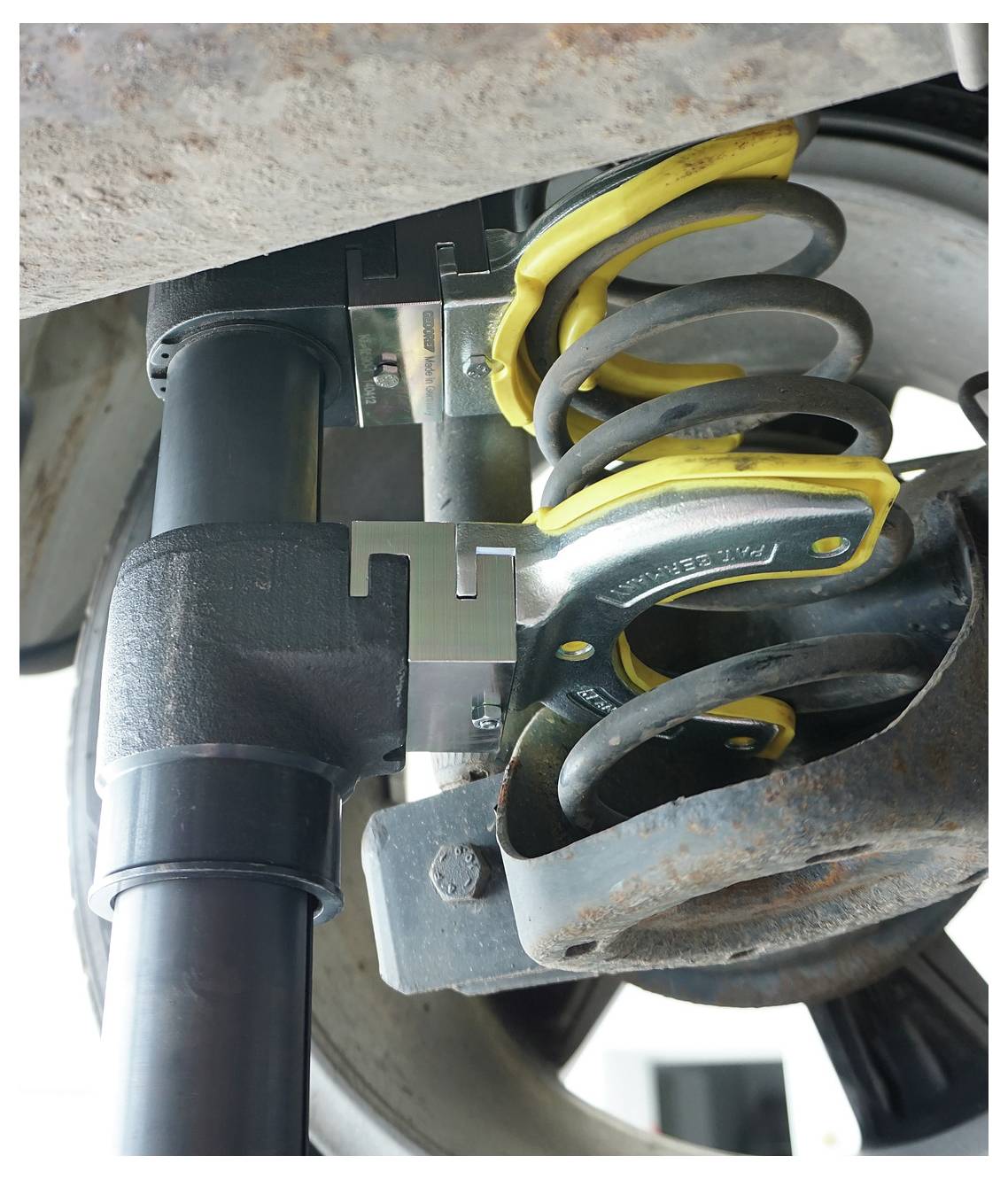 „Eine Nahaufnahme eines Fahrzeugsuspensionssystems, das einen Federkompressor zeigt, der verwendet wird, um die Spiralfeder für Wartungsarbeiten zu komprimieren.