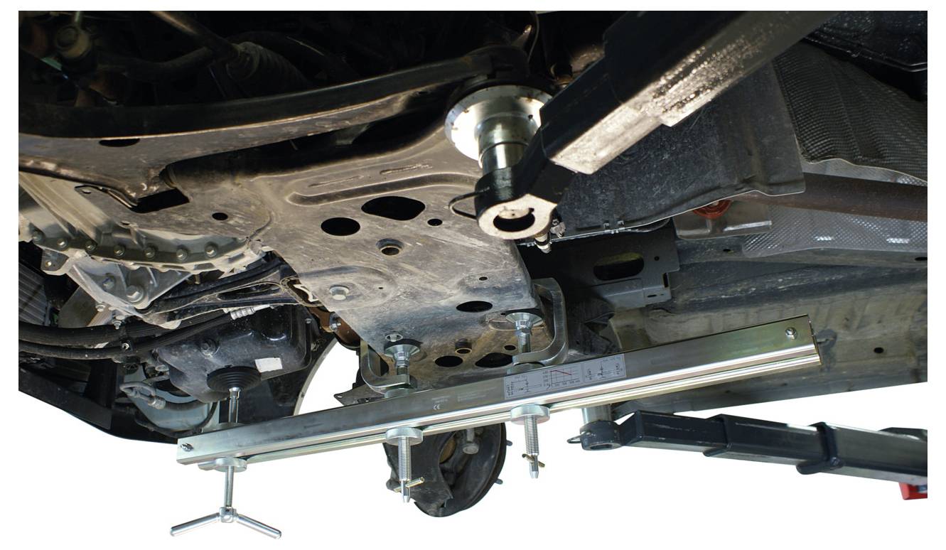 Autobahn mit angebrachtem Werkzeug zur Ausrichtung oder Reparatur; Unteransicht mit Metallrahmen, Aufhängung und rotierendem Werkzeug in Gebrauch.