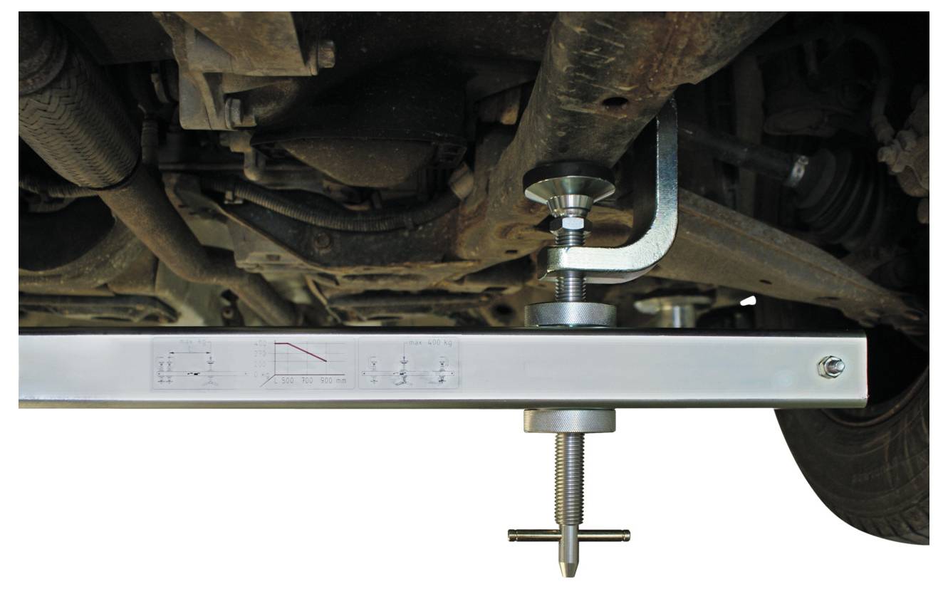 Das Fahrwerk eines Autos mit einem Querträger und einem verstellbaren Spannwerkzeug, wahrscheinlich zum Messen oder Ausrichten von Komponenten.