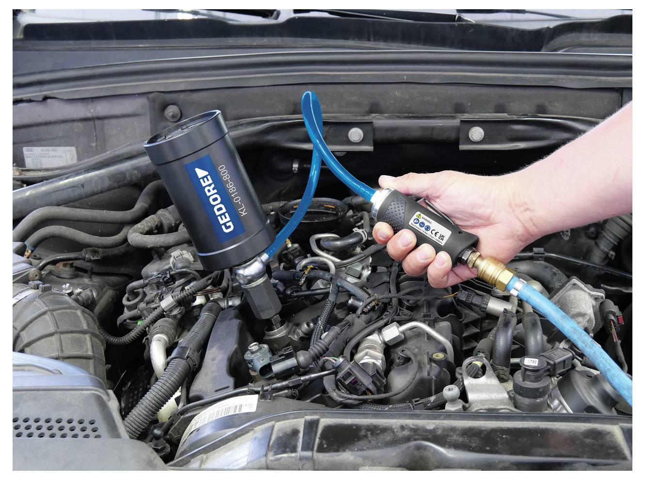 Motorenreinigung läuft mit GEDORE-Ausrüstung; eine Hand hält ein Werkzeug, das über einen blauen Schlauch mit dem Motor verbunden ist.