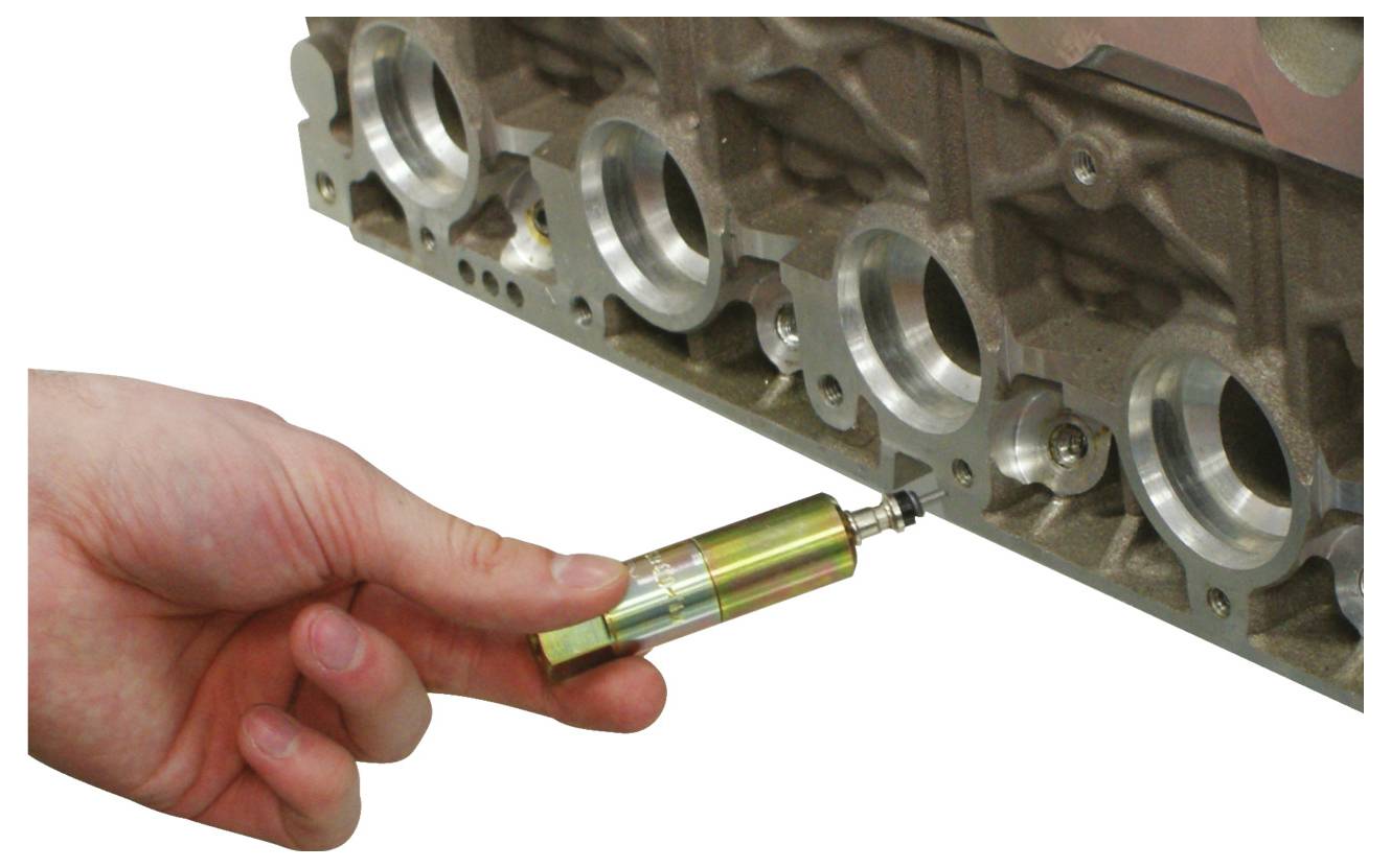 Eine Hand benutzt ein kleines zylindrisches Werkzeug, um die Ventilführungen eines Motorblocks auszurichten. Das Werkzeug passt genau, was auf Wartung oder Montage hindeutet.