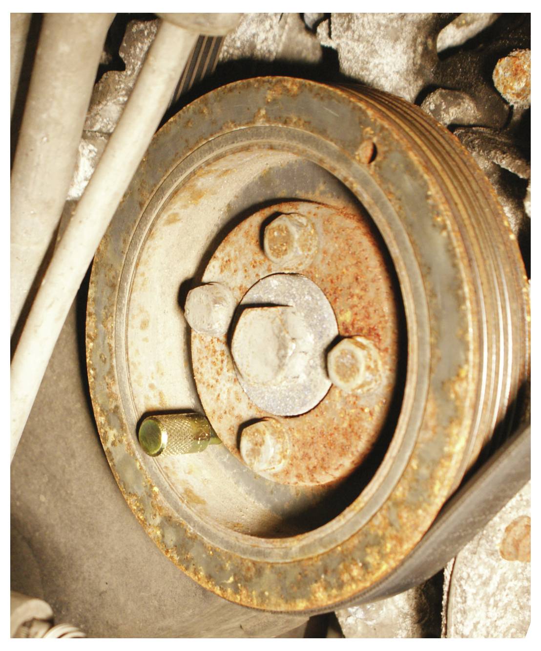 Rostige Automotiv-Riemenscheibe mit korrodierten Bolzen und einer strukturierten Oberfläche, vor einem staubigen, metallischen Hintergrund.