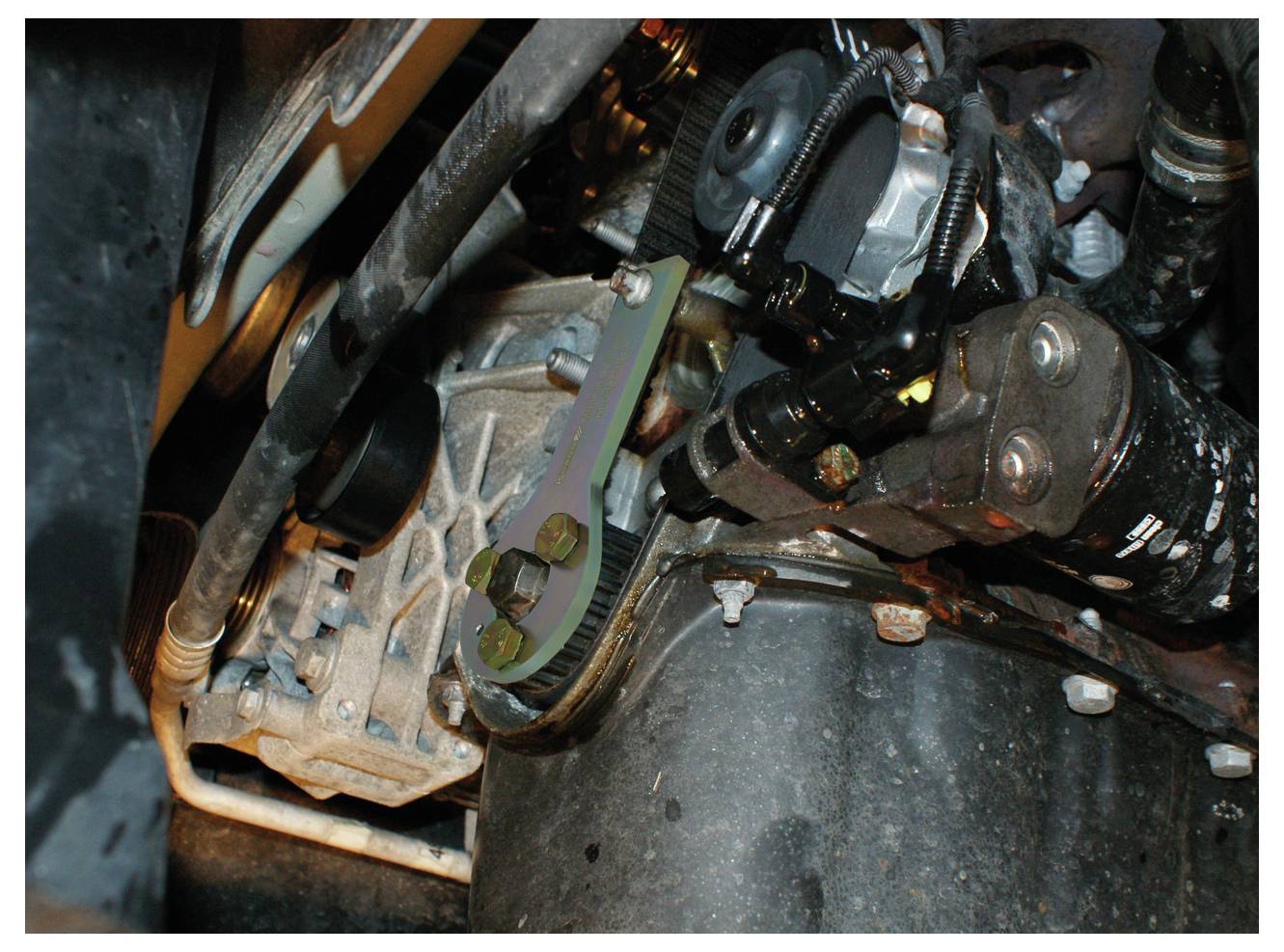 Nahaufnahme eines Motorraums mit verschiedenen mechanischen Komponenten, darunter Riemen, Bolzen und metallische Teile.