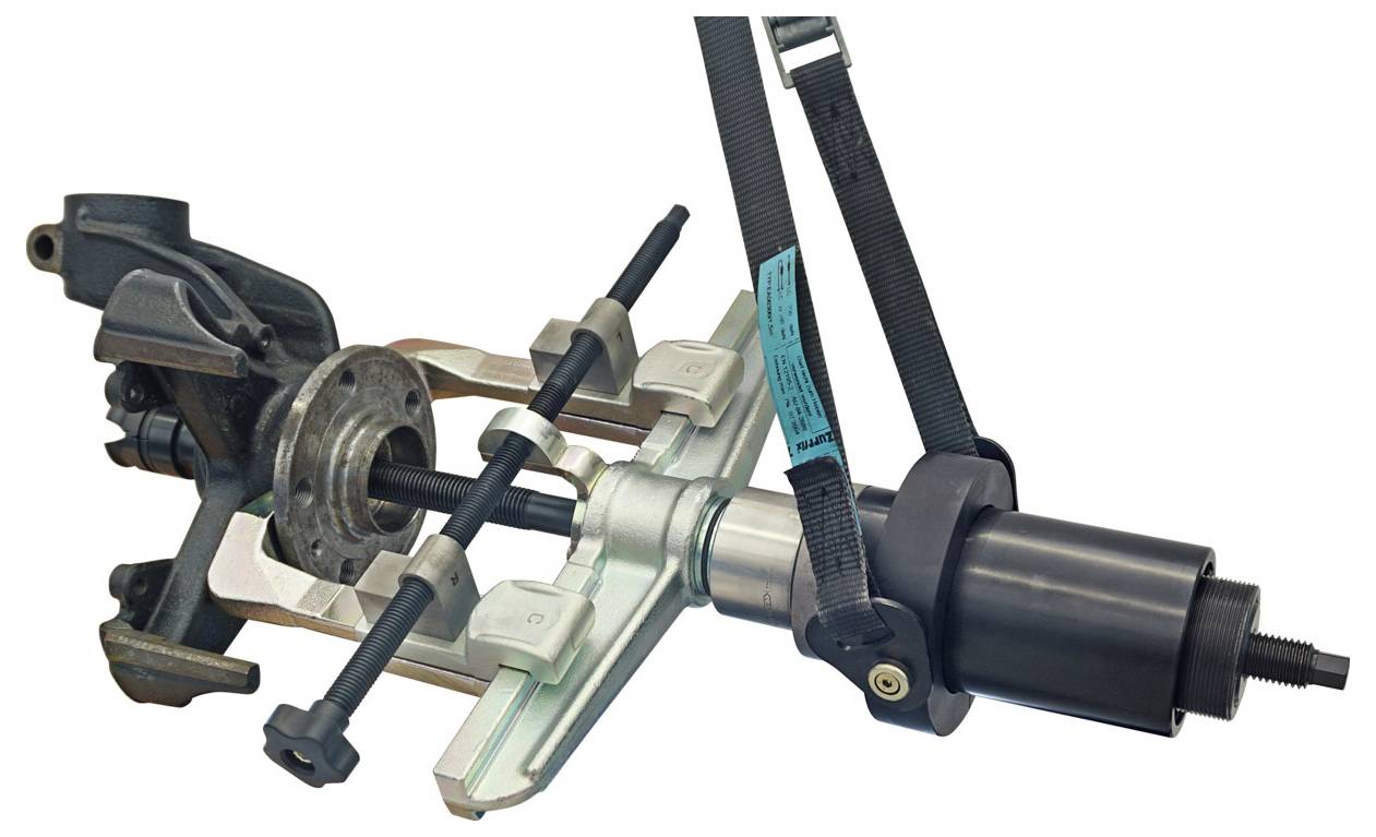 Ein Hydraulik-Naben-Abzieher-Werkzeug, das eine Radnabe entfernt. Das Werkzeug besteht aus einem schwarzen Zylinder und verschiedenen Metallkomponenten, die einen sicheren Griff gewährleisten.