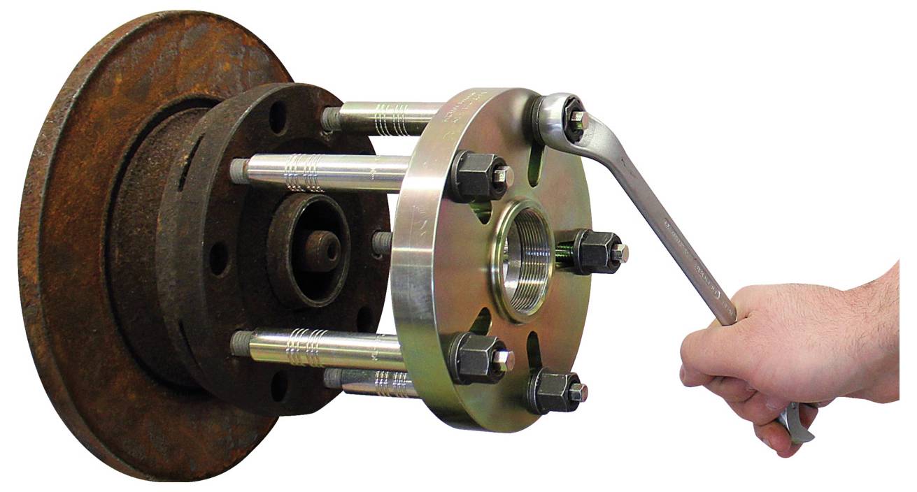 Eine Hand benutzt einen Schraubenschlüssel, um ein Radnaben-Abzieher-Werkzeug an einer rostigen Radnaben-Baugruppe einzustellen und zeigt dabei eine Kfz-Reparatur.