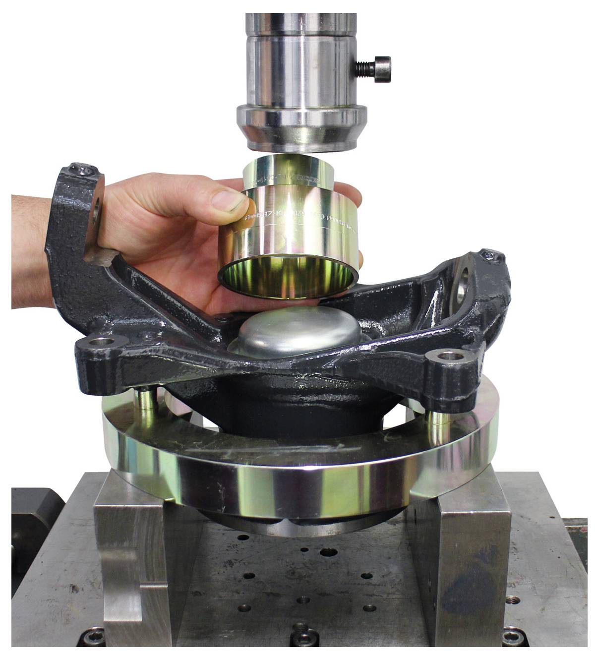 Eine Hand hält eine Metallhülse über eine Automobillagerbaugruppe und Gehäusestruktur auf einem Montagestativ und veranschaulicht einen Montagevorgang.