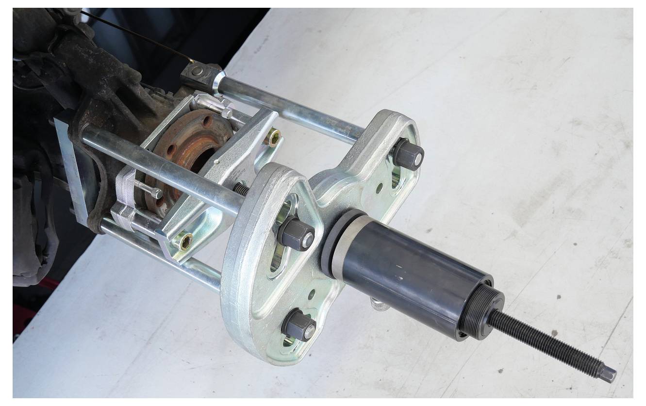 Ein Metallwerkzeuggerät ist an einem Autoteil befestigt, wahrscheinlich Teil eines Fahrzeugreparatur- oder Montageprozesses. Das Werkzeug hat Bolzen und eine zylindrische Komponente.